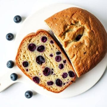 Fresh blueberry bread slice with blueberries on white plate, perfect for breakfast or snack.