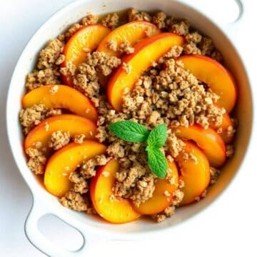 Fresh peach crisp with crumb topping and mint garnish in a white baking dish.