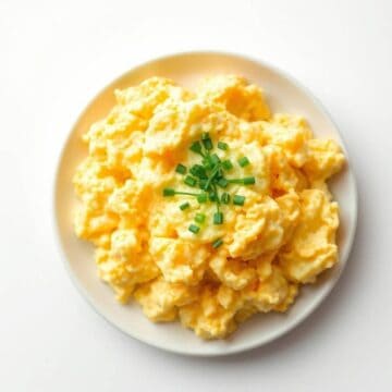 Fluffy scrambled eggs garnished with fresh chopped green onions on a white plate.